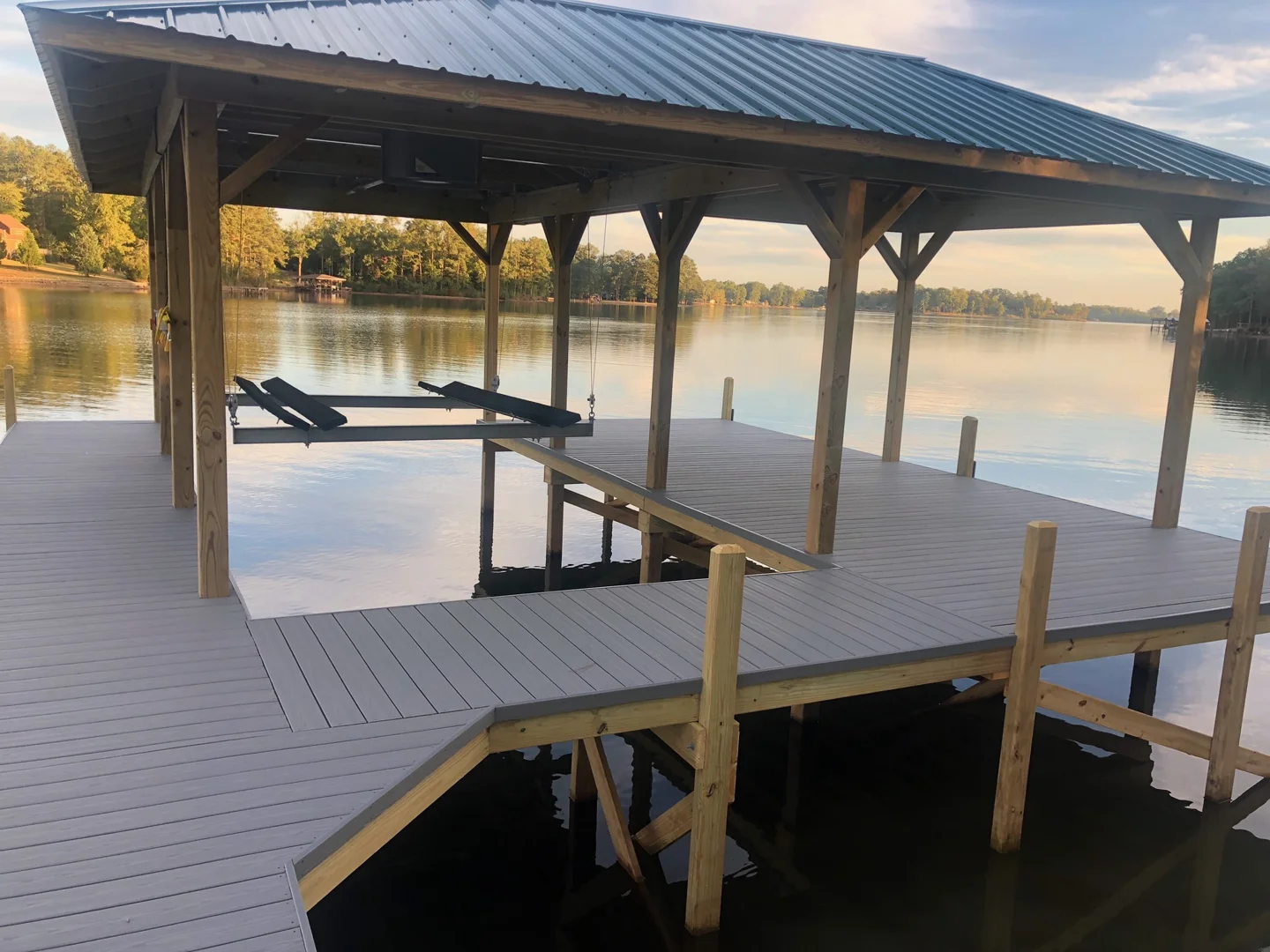 Covered dock and boat lift beside calm water in warm evening light